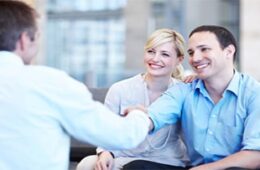 Smiling young couple shaking hands with their property consultant